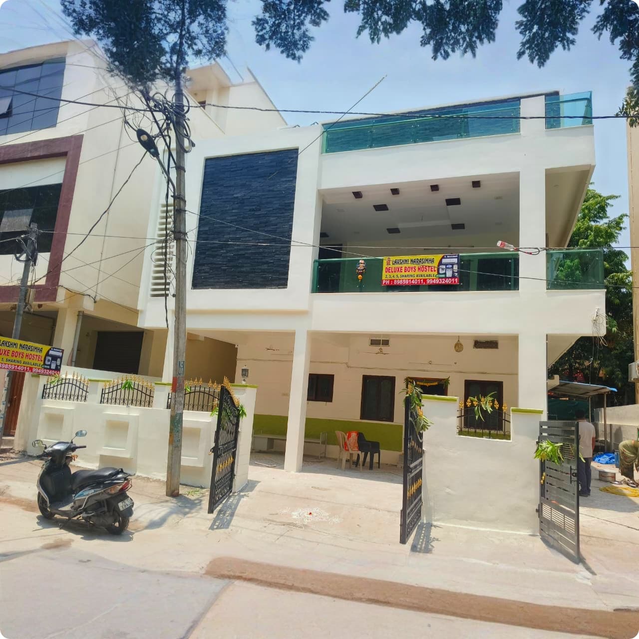 White multi-story building with black stone accents and signage for Lakshmi Narasimha Boys Hostel.