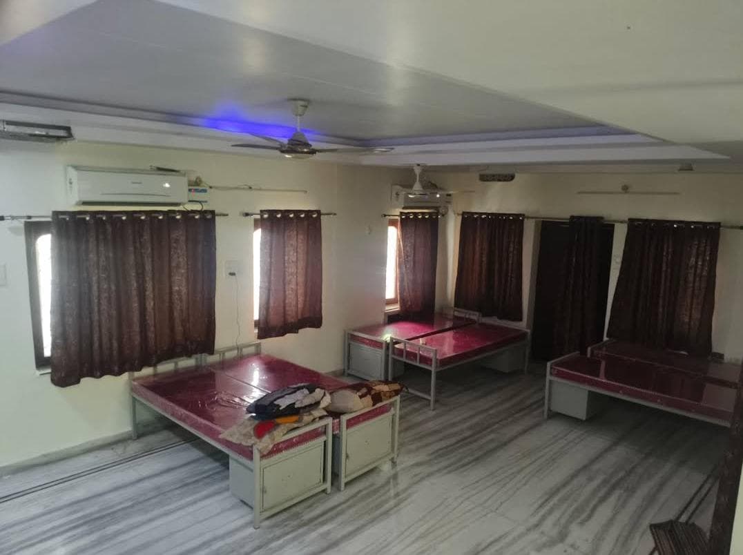 Dormitory room with metal beds, red mattresses, dark brown curtains, and a polished marble floor.