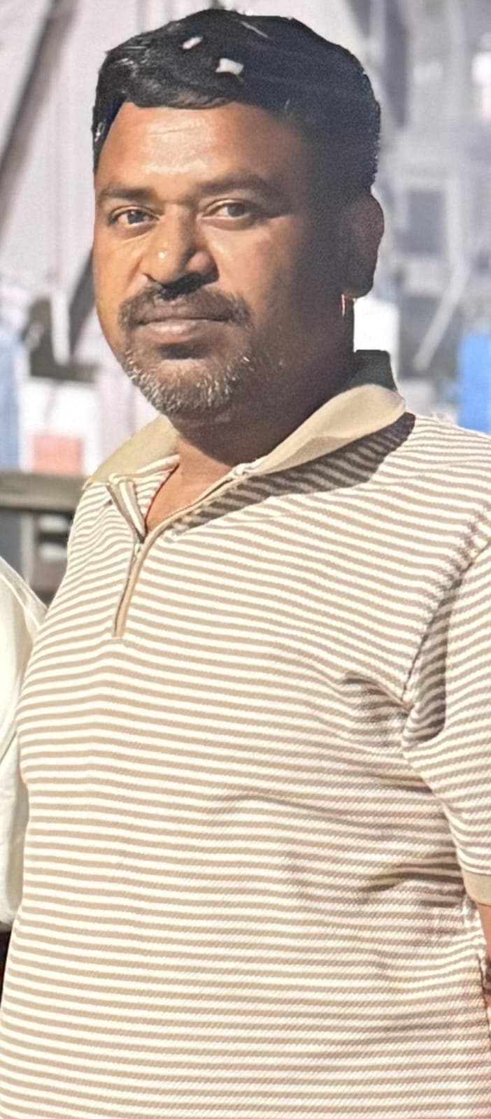 Man with dark hair and a mustache wearing a tan and white striped polo shirt.